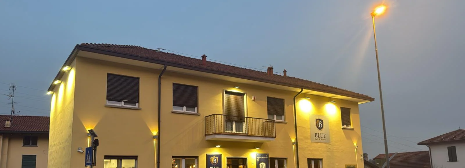 La casa gialla del Blue la sera, con le luci accese e l'insegna
